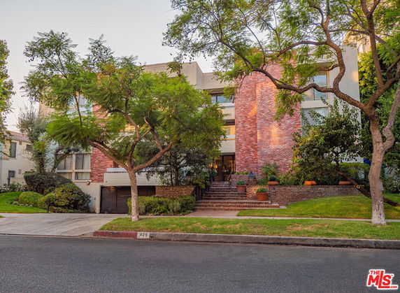 Front view of a multi-story building with a brick facade and large trees in front.
