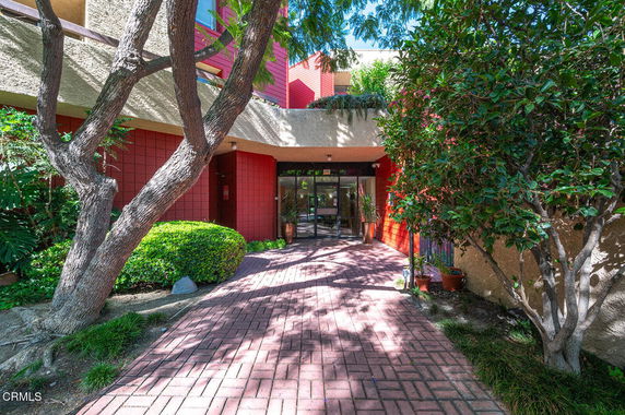 Front view of a building entrance with red wall accents and surrounding greenery.