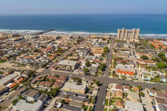 Aerial view of a residential area near the ocean with a pier, showing rows of houses and a large apartment building by the beach.