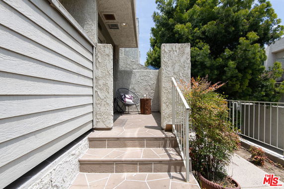 Front view of a house with stairs leading to an entrance and a small seating area.
