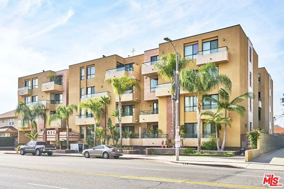 Front view of a modern multi-story apartment building with balconies and palm trees.