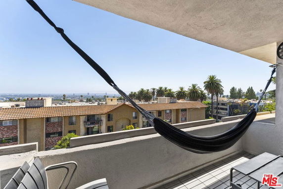 View from a balcony with a hammock overlooking other buildings and palm trees.