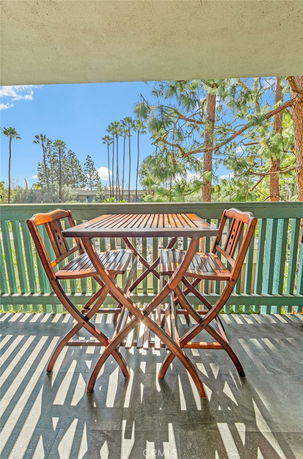 View of surrounding trees and buildings from a balcony with wooden furniture.