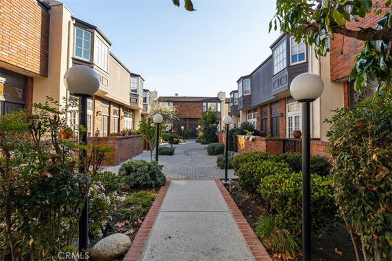 Front view of two-story townhouses with brick and beige exteriors along a landscaped walkway.