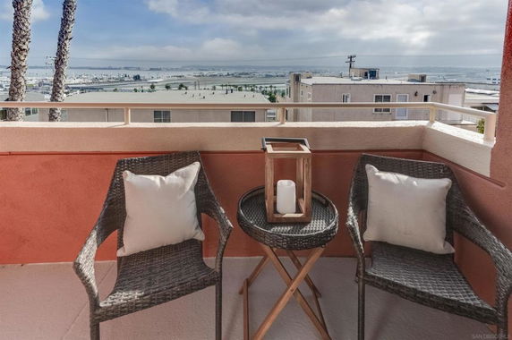 View from a balcony with chairs overlooking buildings and a large body of water in the distance.