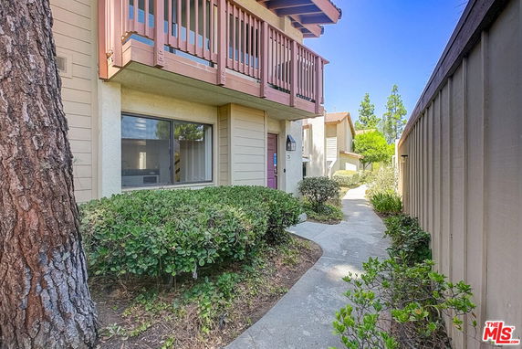 Front view of a multi-level house with a wooden balcony and paved walkway.
