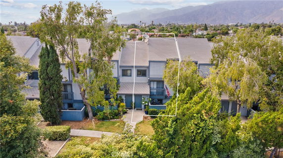 Front view of a multi-story townhouse with trees and plants in front.