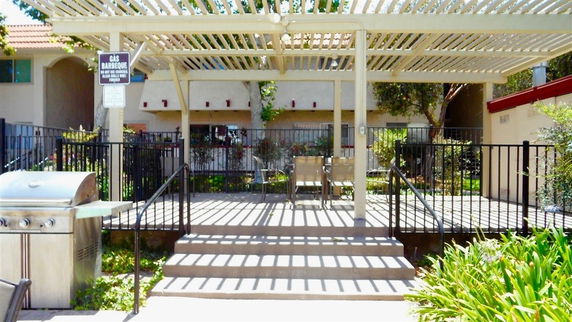 Outdoor patio area with a pergola and gas barbecue grill.