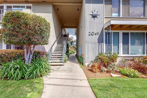 Front view of a multi-story building with external staircase and landscaped surroundings.