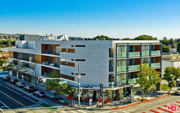 Front view of a multi-story modern building with glass balconies and a street-level retail area.