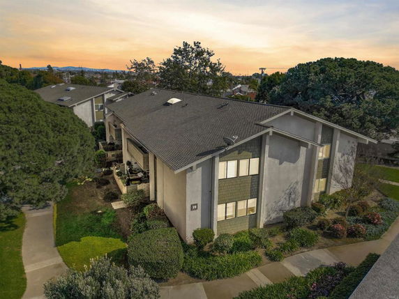 Aerial view of a two-story building with a sloped roof and surrounding greenery.