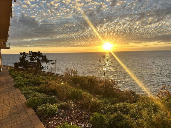 View of the ocean at sunset with a house on the left side.