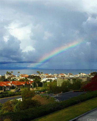 Panoramic view of houses and ocean under a cloudy sky with a rainbow.