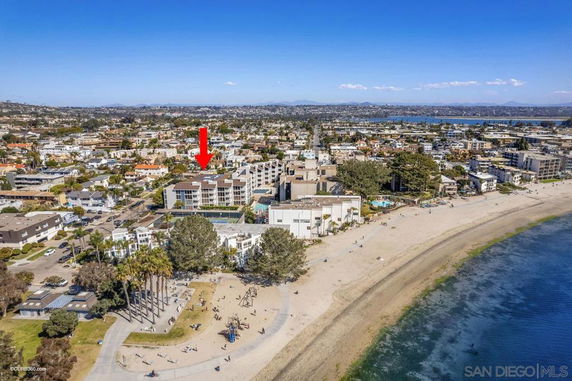 Aerial view of a residential area near a beach with a prominent building marked by a red arrow.