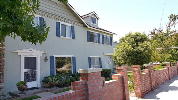Front view of a two-story house with blue shutters and a brick fence.