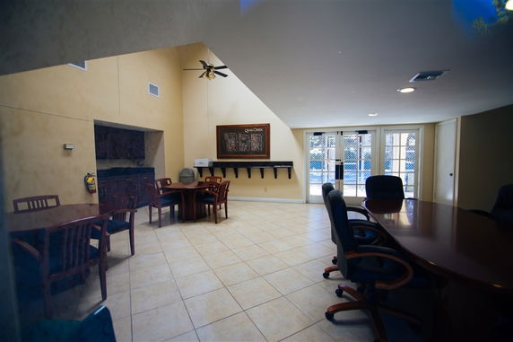 Interior view of a recreational room with tables and chairs, featuring large windows and a high ceiling.