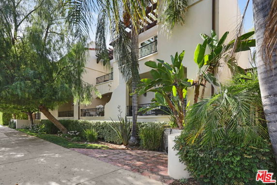 Front view of a multi-story residential building with balconies and lush greenery.
