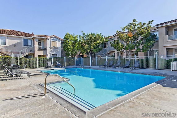 Outdoor swimming pool area surrounded by two-story buildings with balconies.