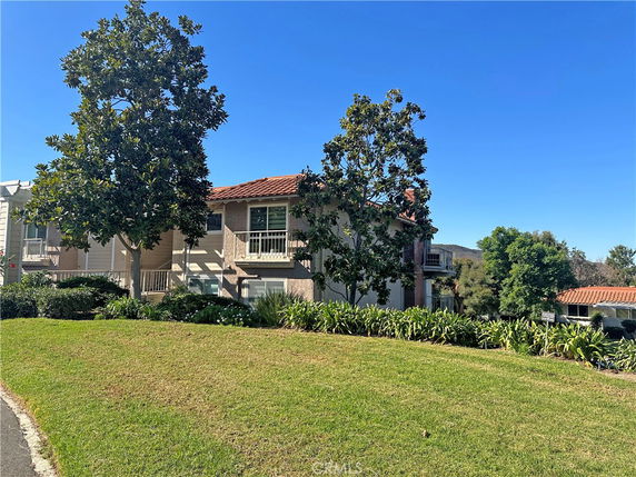 Front view of a two-story house with a tiled roof and multiple trees in the yard.