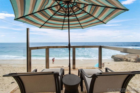 View of ocean from a deck with chairs and an umbrella.