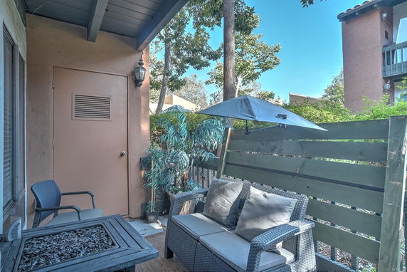 Outdoor patio area with seating and privacy fence, view of trees and neighboring building.