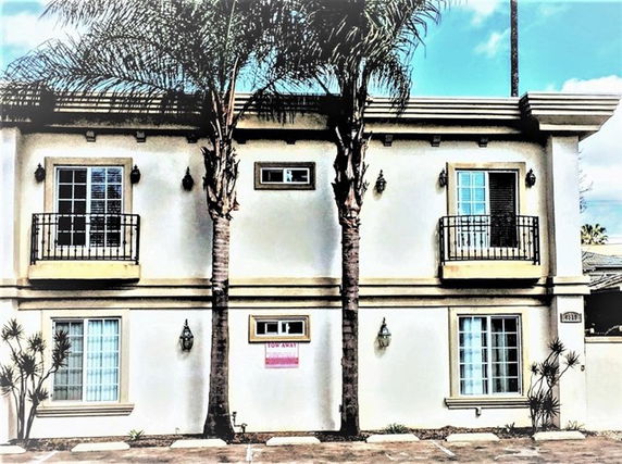 Front view of a two-story building with balconies and palm trees.