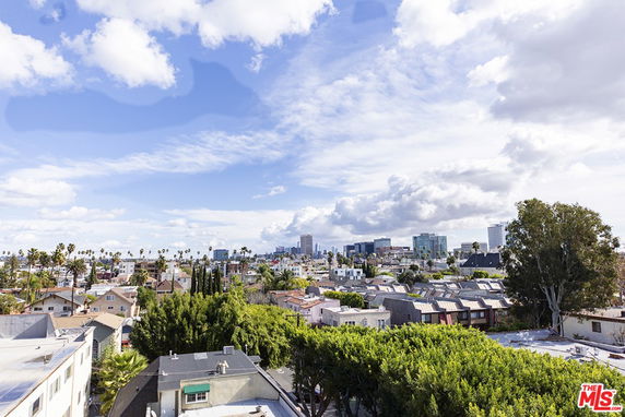 Panoramic view of a suburban neighborhood with houses and distant city skyline under a partly cloudy sky.