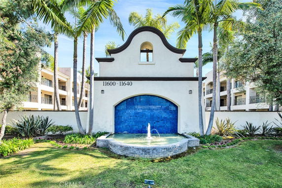 Front view of a building with a decorative archway and a fountain in front.