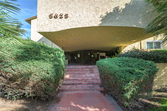 Front view of a building entrance with an arched walkway and red-tiled pathway.