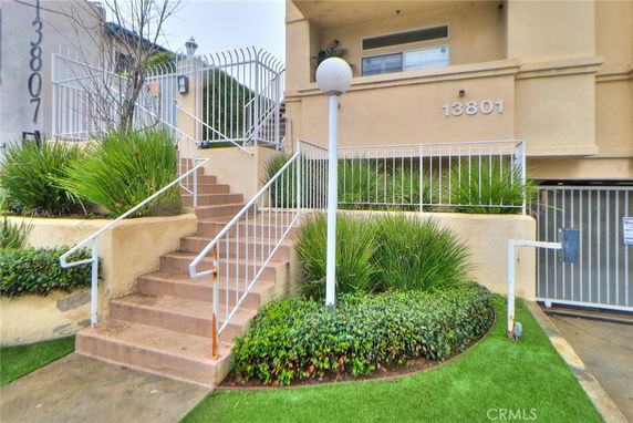 Front view of a multi-story residential building entrance with stairs and greenery.