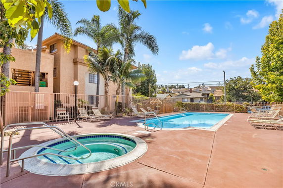 Outdoor swimming pool area with lounge chairs and a hot tub beside a building.
