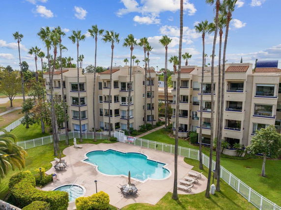 Apartment complex with swimming pool surrounded by palm trees and grassy area.