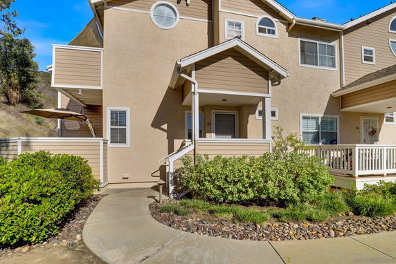 Front view of a multi-story house with beige siding, small porch, and circular window.