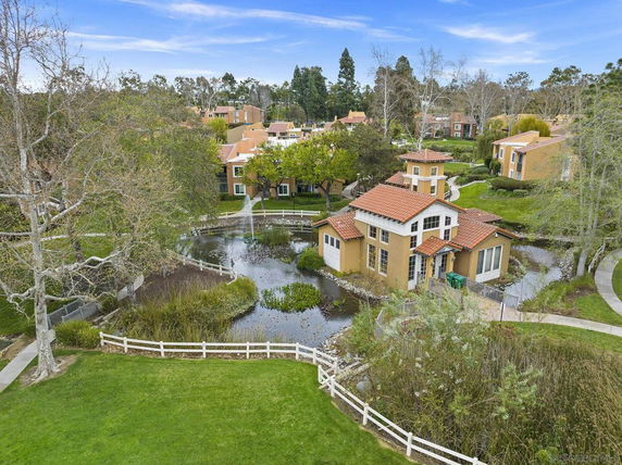 Aerial view of a cluster of residential buildings with red-tiled roofs, surrounded by greenery and a pond.