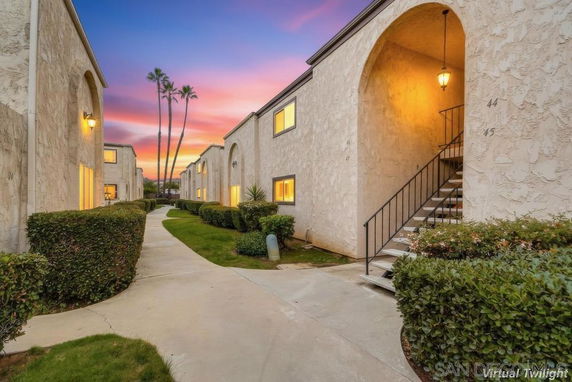 Front view of a multi-unit building with exterior staircases and arched entryways at sunset.