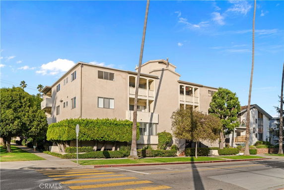 Front view of a multi-story residential building with balconies and surrounded by trees.
