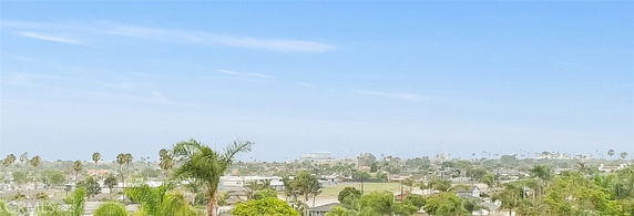 Wide view of a residential area with distant trees and buildings under a clear blue sky.