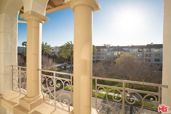 Panoramic view from a balcony overlooking a residential area with palm trees and a modern building.