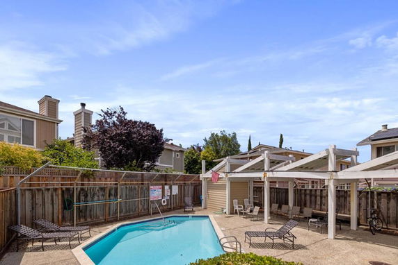 Outdoor swimming pool area surrounded by wooden fencing and nearby residential houses.