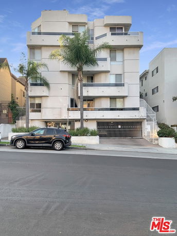 Front view of a multi-story residential building with balconies and a parking area underneath.