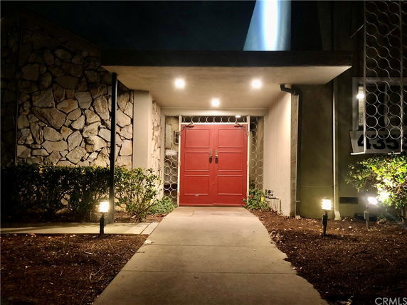 Front view of a building entrance with a red door and stone wall.