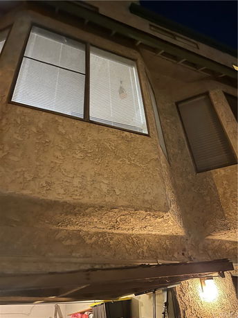 Upward view of a house facade with textured walls and windows.