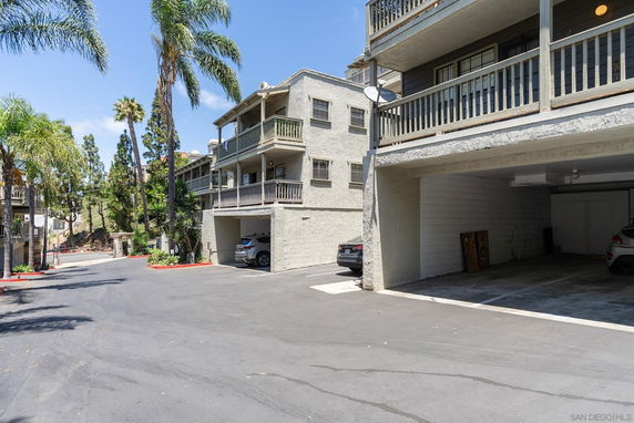 Outdoor parking area under a residential building with cars parked.