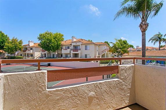 View from a balcony overlooking a residential area with several two-story buildings and a tennis court.
