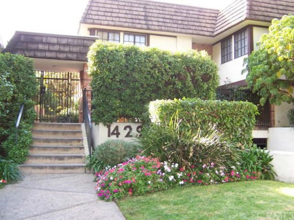 Front view of a multi-story building with a shingled roof and garden at the entrance.