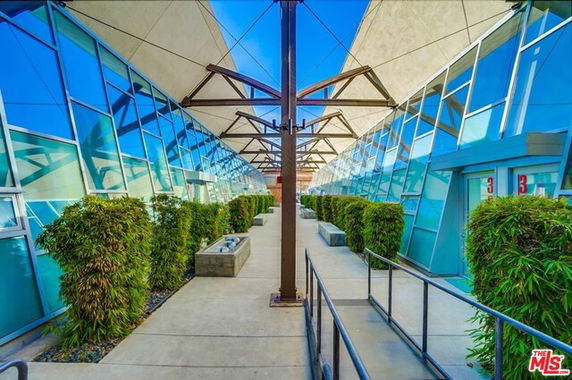 Front view of a modern building with slanted glass facades and plants lining the entrance walkway.