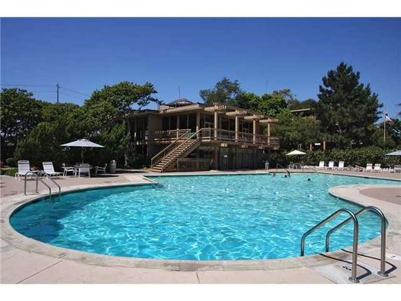 Outdoor swimming pool with surrounding lounge chairs and a building in the background.