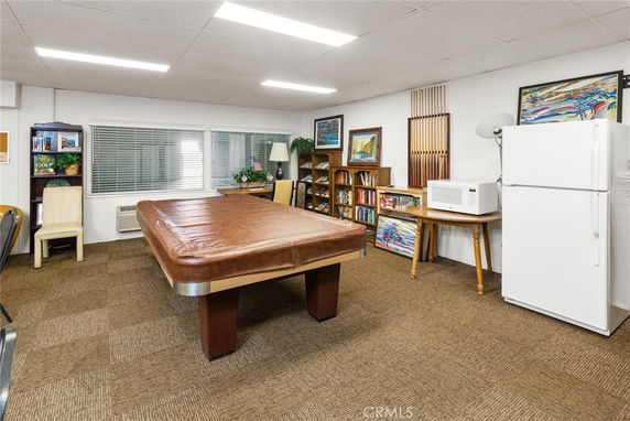 Room with a covered pool table, bookshelves, refrigerator, and microwave