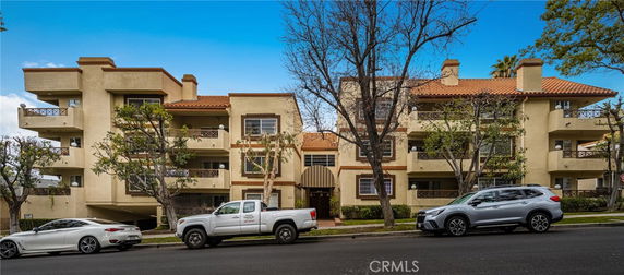 Front view of a multi-story residential building with balconies and parked cars in front.