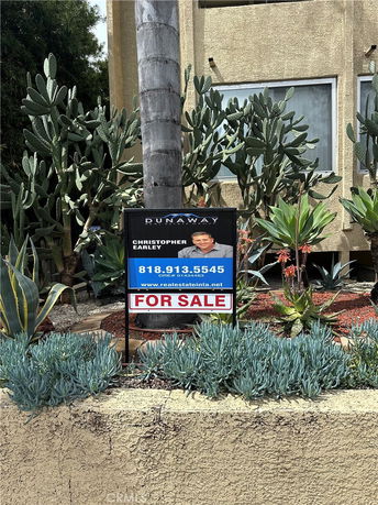 Front view of a building with a 'For Sale' sign and desert plants.
